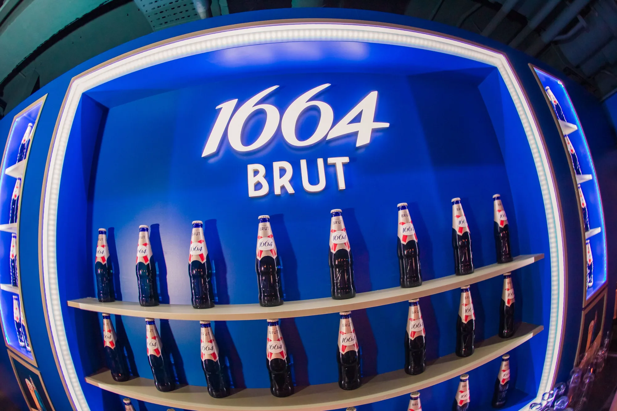 The 1664 Brut back bar, lit blue, with bottles on curved shelves