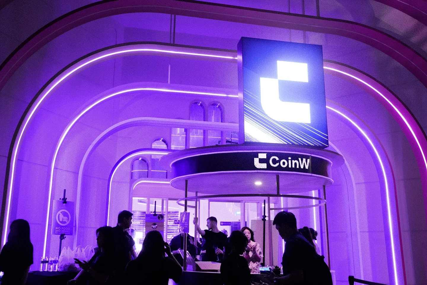 The entrance, a revolving door under an arched light frame and a CoinW cube