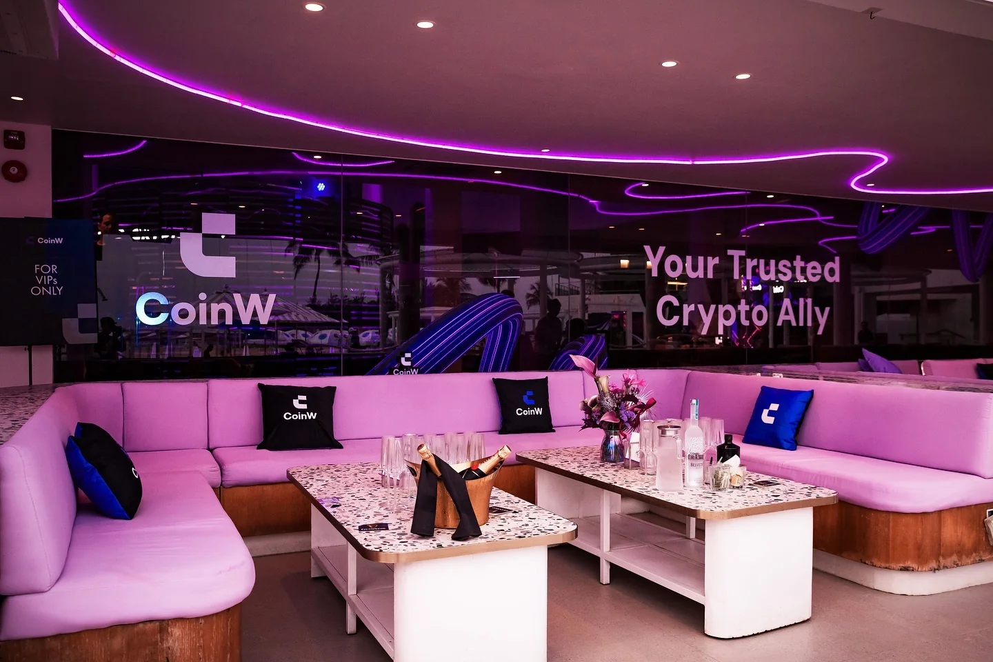 A VIP lounge with CoinW cushions and a Your trusted crypto ally screen